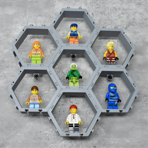 Seven LEGO minifigures are showcased in a Chatelet Manufacturing Hexagon Wall Display—compatible with Lego figures, customizable, and made in the USA—each in its own interlocking hex block on a gray surface.