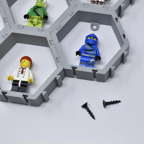 Three minifigures are displayed in a Chatelet Manufacturing Hexagon Wall Display Compatible With Lego Figures; two black screws rest on the white surface.