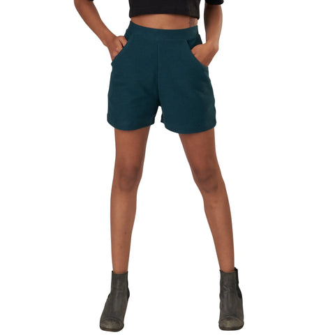 A person stands with hands in pockets, wearing Spiritex | Sustainable Apparels Betty Hi Waist Shorts. Only the lower body is visible against a white background.