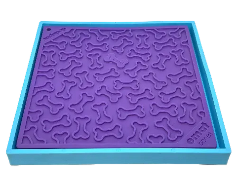 A square, purple silicone mat with raised bone shapes sits inside a light blue tray. This is the SodaPup Hold Em Suction Cup Holder, designed for EBowls, ETrays, and EMats as a creative dog bowl holder.