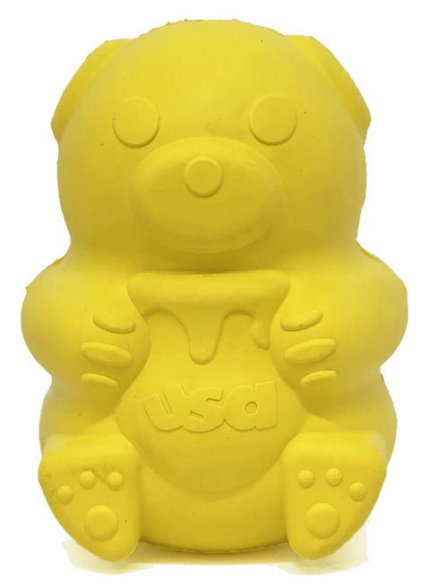 The SodaPup Honey Bear EDispenser is a durable yellow rubber bear-shaped treat dispenser, sitting upright with a usa-labeled honey pot, featuring round ears, dotted eyes and nose, and paw prints on its feet.