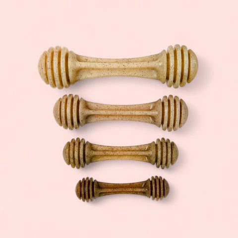 Four Honey Bone EChew Ultra Durable Nylon Dog Chew Toys by SodaPup, designed for power chewers with grooves at both ends, are displayed vertically on a light pink background.