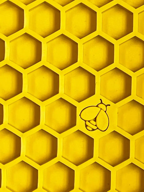 The Honeycomb Design Emat Enrichment Lick Mat by SodaPup features a yellow honeycomb pattern with hexagonal cells and an outlined bee in the lower right—ideal inspiration for your dog’s next enrichment toy.