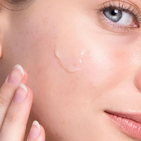 A close-up of a woman applying Open Formula’s Hyaluronic Acid Gel to her cheek, targeting dry skin. Her complexion looks smooth, and she has light-colored eyes and natural, clean nails.