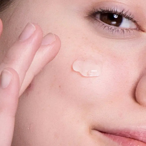 A close-up of someone applying Open Formula Hyaluronic Acid Gel to their cheek, revealing smooth skin—ideal for hydrating dryness and minimizing the look of lines and wrinkles.