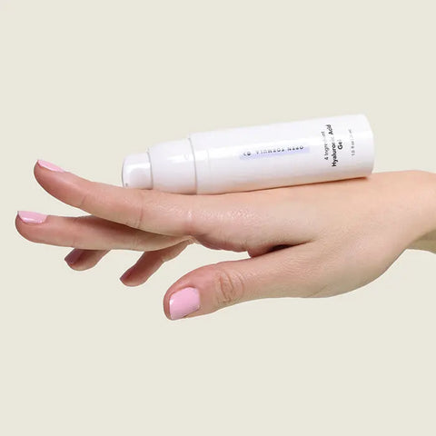 A hand with light pink nail polish holds Open Formula Hyaluronic Acid Gel across the fingers, ready to hydrate dry skin and smooth lines and wrinkles, against a pale background.