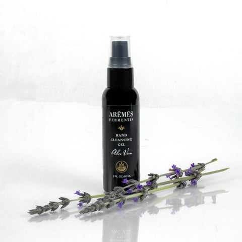A black AREMES FERMENTIS Aloe Vera Hand Cleansing Gel bottle stands upright on a white surface, with purple lavender sprigs in front—emphasizing this hydrating hand gel’s sanitizing power.