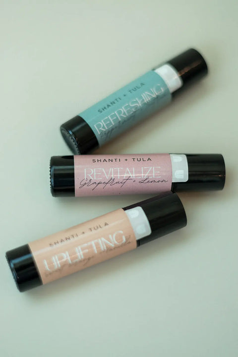 Three Shanti + Tula Hydrating Natural Lip Oils with rollerball applicators are arranged diagonally on a light surface. Each features a pastel label, combining clean beauty with easy use. Made in Utah.