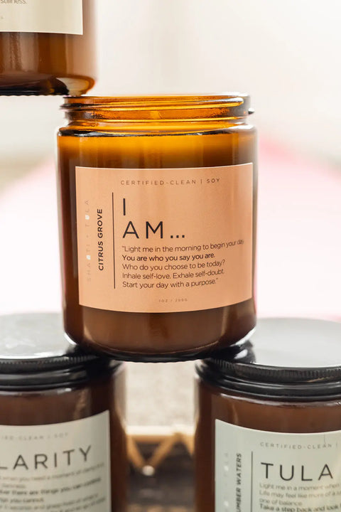 The “I AM…” Affirmation Candle by Shanti + Tula is a brown glass soy candle with an inspirational label, Citrus Grove scent, and Certified Clean; two other mindfulness candles are partially visible below.