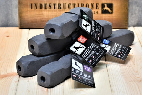 Four black, hexagonal Indestructibone Kennel Pack chew toys by Bulletproof Pet Products Inc, in four sizes, stacked on wood. Each toy sports dog and brand logos—ideal for aggressive chewers with a matching logo sign in the background.