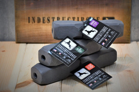 Three black, hexagonal Indestructibone Professional Grade Chew Toys (Variety Pack: 1 XL, 1 XL Plus, 1 Mega Max) by Bulletproof Pet Products Inc are stacked on wood with tags. A wooden INDESTRUCTIBONE sign is in the blurred background.