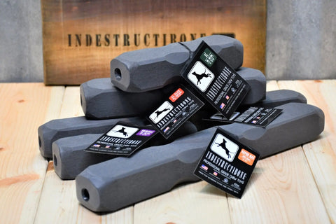 Five gray, hexagonal Indestructibone Ultimate Kennel Pack chew toys by Bulletproof Pet Products Inc in five sizes are stacked on a wooden surface with an INDESTRUCTIBONE sign—USA-made, professional grade for heavy chewers.