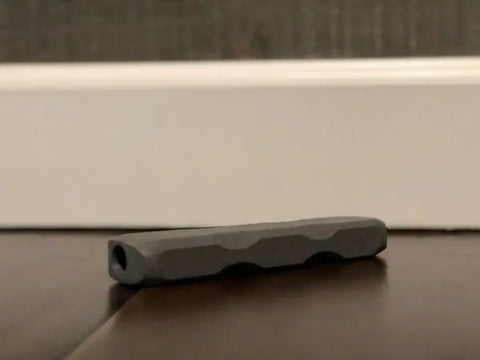 An Indestructibone Professional Grade Mini from Bulletproof Pet Products Inc, designed for dogs up to 15 lbs, lies on a wooden floor near a white baseboard and dark wall.