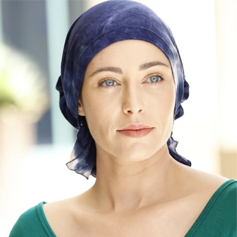 A woman with light eyes and fair skin wears the Elise Scarves - Chemo Beanies® by Chemo Beanies®, paired with a green top. She gazes softly to the side, her calm expression enhanced by a gently blurred serene background.