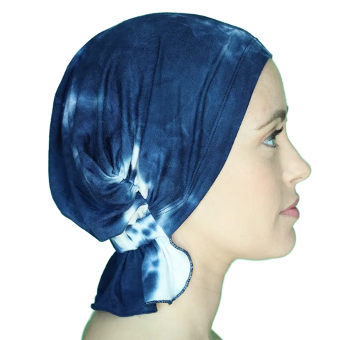 A woman with fair skin in profile wears the Chemo Beanies® Elise blue and white tie-dye chemo beanie, which covers her hair and ties at the back. She faces right against a plain background.