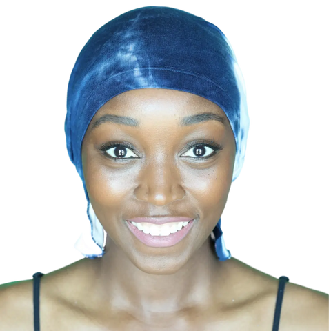 A smiling woman faces forward against a plain white background, wearing the Chemo Beanies® Elise blue tie-dye chemo beanie and a black top.