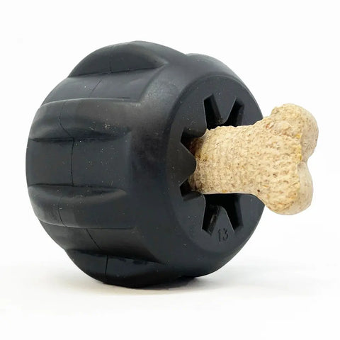 The SodaPup Gear EDispener Durable Rubber Treat Holder and Chew Toy is shown in black with grooves, holding a beige bone-shaped treat partially inserted into its opening against a plain white background.