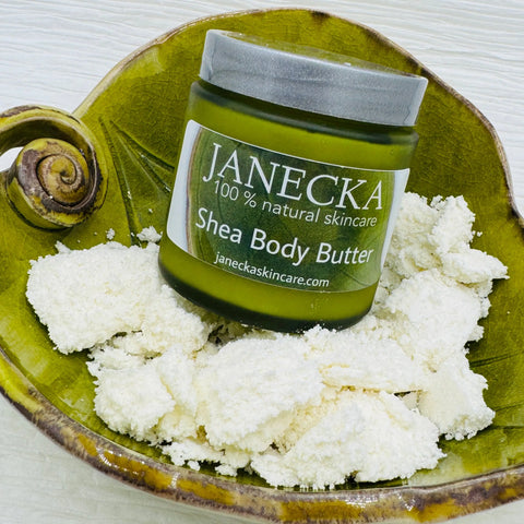 A green jar of Janecka Skincare JANECKA Shea Body Butter sits on a decorative green dish with shea butter chunks, a natural moisturizer ideal for soothing eczema and psoriasis.