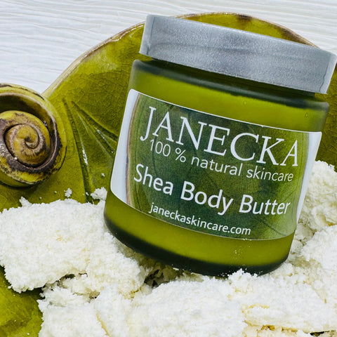 A green jar of Janecka Skincare JANECKA Shea Body Butter sits on a green plate with a snail decoration, surrounded by shea butter chunks—an ideal natural moisturizer for eczema and psoriasis.