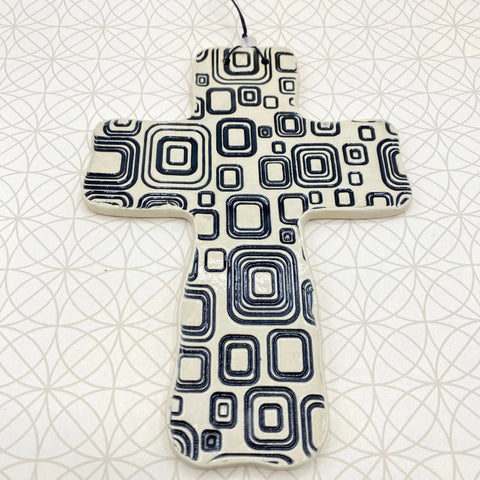 The Janecka Cross of Hope, a handmade black square pottery wall cross by Janecka, features a geometric pattern and is displayed on a white surface—an artisan housewarming gift with unique charm.