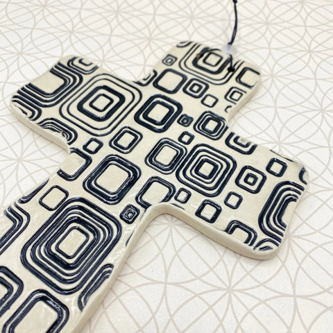 The Janecka Cross of Hope is a handmade black square pottery wall cross on white ceramic, featuring geometric designs—an artisan housewarming gift by Janecka for lovers of unique decorative crosses.