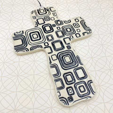 The Janecka Cross of Hope, a handmade pottery wall cross with black concentric squares on white ceramic, makes a unique housewarming gift. From the Janecka brand.