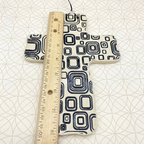 The Janecka Cross of Hope, Black Square Pottery Wall Cross, is shown measured vertically with a wooden ruler. Crafted by Janecka, this artisan cross rests on a white surface—a unique handmade housewarming gift.