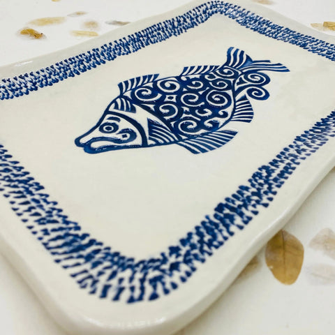 The Janecka JANECKA Blue Fish Tray is a handmade, rectangular white ceramic tray featuring a blue fish with swirl patterns and a blue border—an ideal artisan gift.