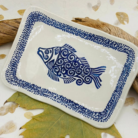 The JANECKA Blue Fish Tray by Janecka is a handmade rectangular pottery tray with a central blue fish motif and decorative blue border, perfect as a unique artisan gift or home decor piece.