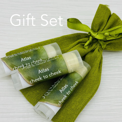 Three JANECKA Atlas Cheek to Cheek Herbal Healing Ointments by Janecka Skincare, made with natural ingredients, sit on a green fabric pouch tied with ribbon. Gift Set is written in white text at the top left of the image.