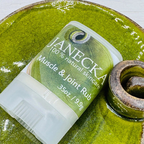 A container of JANECKA Muscle & Joint Rub by Janecka Skincare (.35 oz/9.9g), famed for herbal pain relief, sits on a green ceramic dish with a round decorative handle.