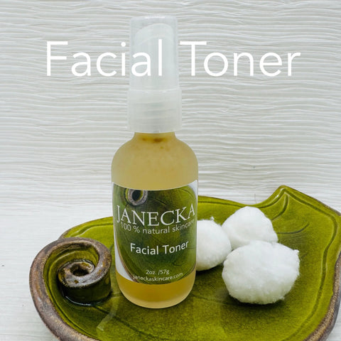 A bottle of JANECKA Facial Toner by Janecka Skincare, made with natural ingredients, rests on a green dish next to two cotton balls. The label features 100% natural skincare and Facial Toner is displayed above the bottle in large text.