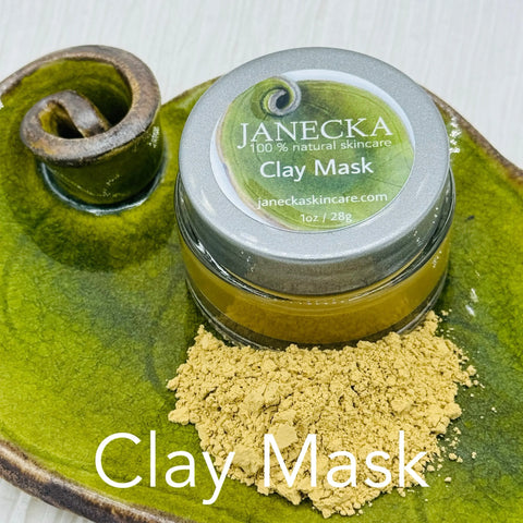 A small jar labeled JANECKA Clay Mask by Janecka Skincare rests on a green ceramic dish next to yellow clay powder, with Clay Mask in white text below, emphasizing its natural ingredients and gentle exfoliating properties.