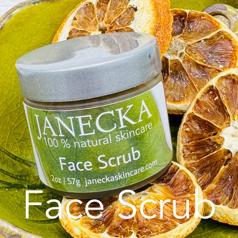 A jar of JANECKA Face Scrub by Janecka Skincare sits on a green dish with dried orange slices. The green and white label is visible, with the words “Face Scrub” overlaid at the bottom of the image.