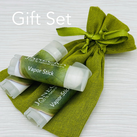 Three JANECKA Herbal Vapor Rub sticks by Janecka Skincare with green labels sit before a matching pouch. Infused with essential oils for organic congestion relief, “Gift Set” appears in the upper left corner.