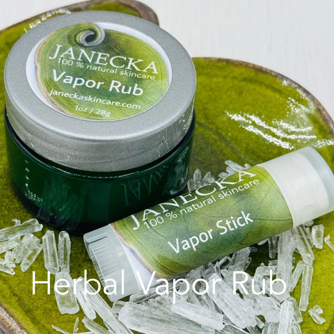 A green glass jar of Janecka Skincare JANECKA Herbal Vapor Rub and a matching stick are shown with herbal crystals on a tray, showcasing this natural congestion relief product. Herbal Vapor Rub is at the bottom.