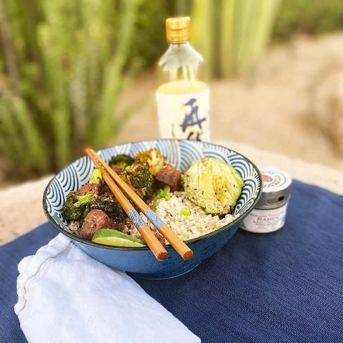A bowl of rice with grilled veggies, beef cubes, and avocado is set outdoors with chopsticks, sauce, and a lime wedge—all elevated by Gustus Vitae’s Japanese Seasoning Gift Set: Tastes of Japan artisanal spice blends.