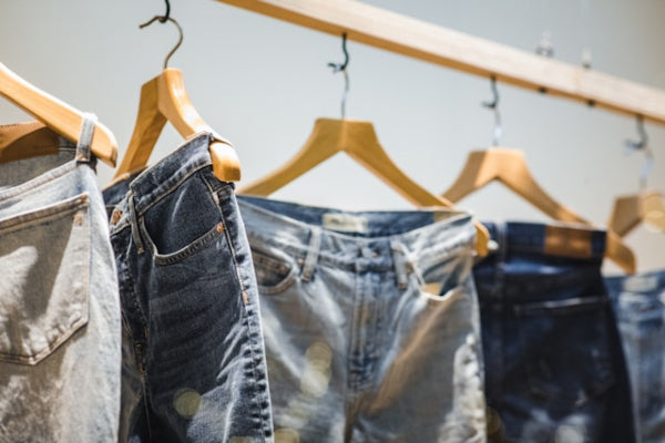 Multiple pairs of jeans hanging on wooden hangers against a neutral background