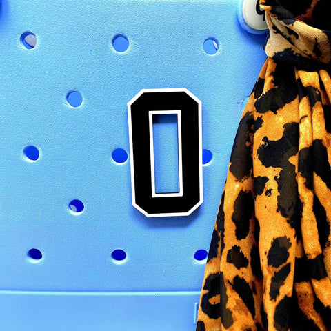 A BOGLETS - Jersey Sports Uniform T-Shirt Number 0 magnet by Chatelet Manufacturing is displayed on a blue perforated board beside brown and black leopard print fabric, perfect for creating custom bag charms or tote accessories.