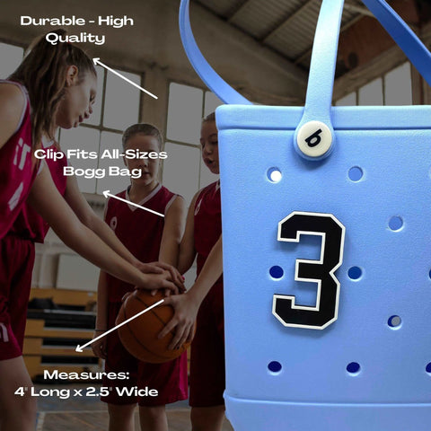 A close-up of a blue BOGLETS - Jersey Sports Uniform T-Shirt Number by Chatelet Manufacturing features a white button and number 3, shown beside young basketball players. Highlights include durability, clip feature, and stylish jersey bag charms.