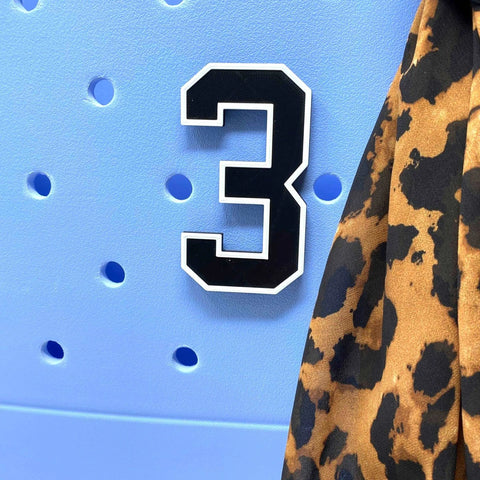 A Chatelet Manufacturing BOGLETS - Jersey Sports Uniform T-Shirt Number 3 in black and white is attached to a light blue perforated board, with brown and black leopard-print fabric hanging on the right edge.