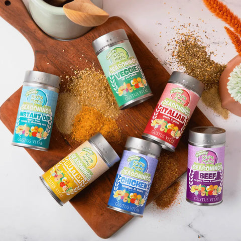Six colorful Gustus Vitae Kid’s Menu: Butter: And House Favorite Spices tins, made with all-natural ingredients, are displayed on a wooden board and white surface, surrounded by scattered seasonings and a small potted plant.