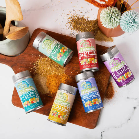 Six vibrant Gustus Vitae Kid’s Menu: Beef: Burgers, Tacos & Meatballs Seasoning jars sit on a wooden board with scattered spices, utensils, and a small vase—each fun label spotlights this all-natural blend made just for kids.