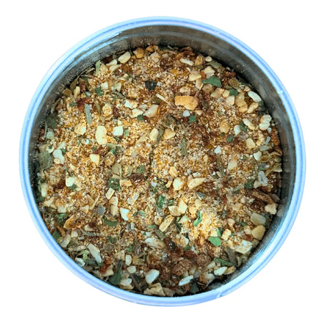 A round metal container of Gustus Vitae Kid’s Menu: Beef: Burgers, Tacos & Meatballs Seasoning, a coarse blend with dried herbs, spices, and bits of garlic or onion, viewed from above on a white background.
