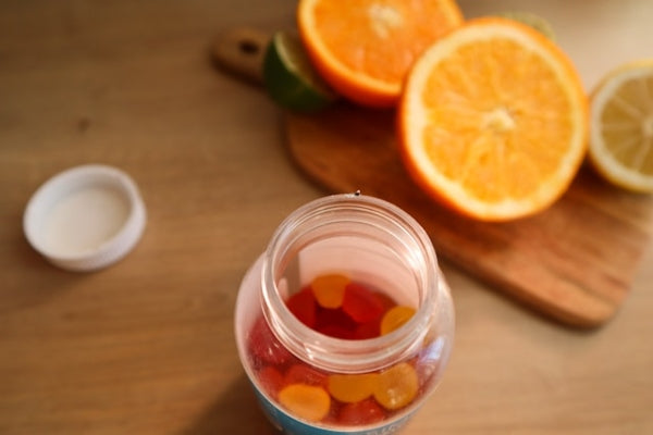 Jar of gummy bears on a wooden surface with sliced oranges and a small container of salt.