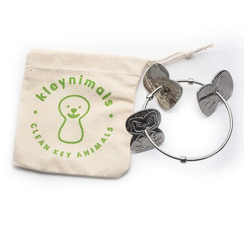 The Kleynimals Stainless Steel Rattle by Kleynimals, with three animal-shaped keys, sits beside a beige pouch with a green logo and Kleynimals Clean Key Animals, making it an ideal eco-friendly baby gift.