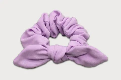 The Goodnighties Knotted Bow Scrunchie, in light purple thermoregulating fabric, is shown on a white background—an elegant American-made hair accessory perfect for any occasion.