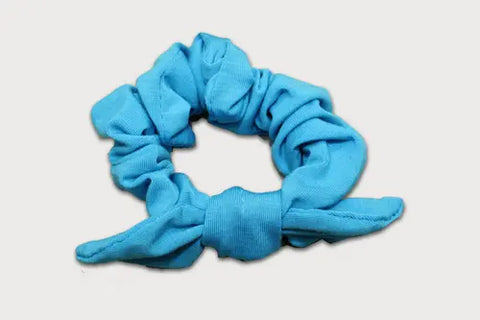 The Goodnighties Knotted Bow Scrunchie in light blue, crafted from thermoregulating fabric, features a bow detail on one side and is displayed against a white background.