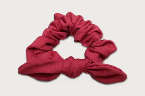 The Goodnighties Knotted Bow Scrunchie, crafted from thermoregulating fabric in red, is an American-made hair accessory that offers style and comfort for everyday wear. Displayed on a plain light background.