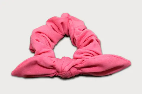 The Goodnighties Knotted Bow Scrunchie is a pink, American-made hair accessory with two pointed ends like bunny ears, shown on a plain white background.